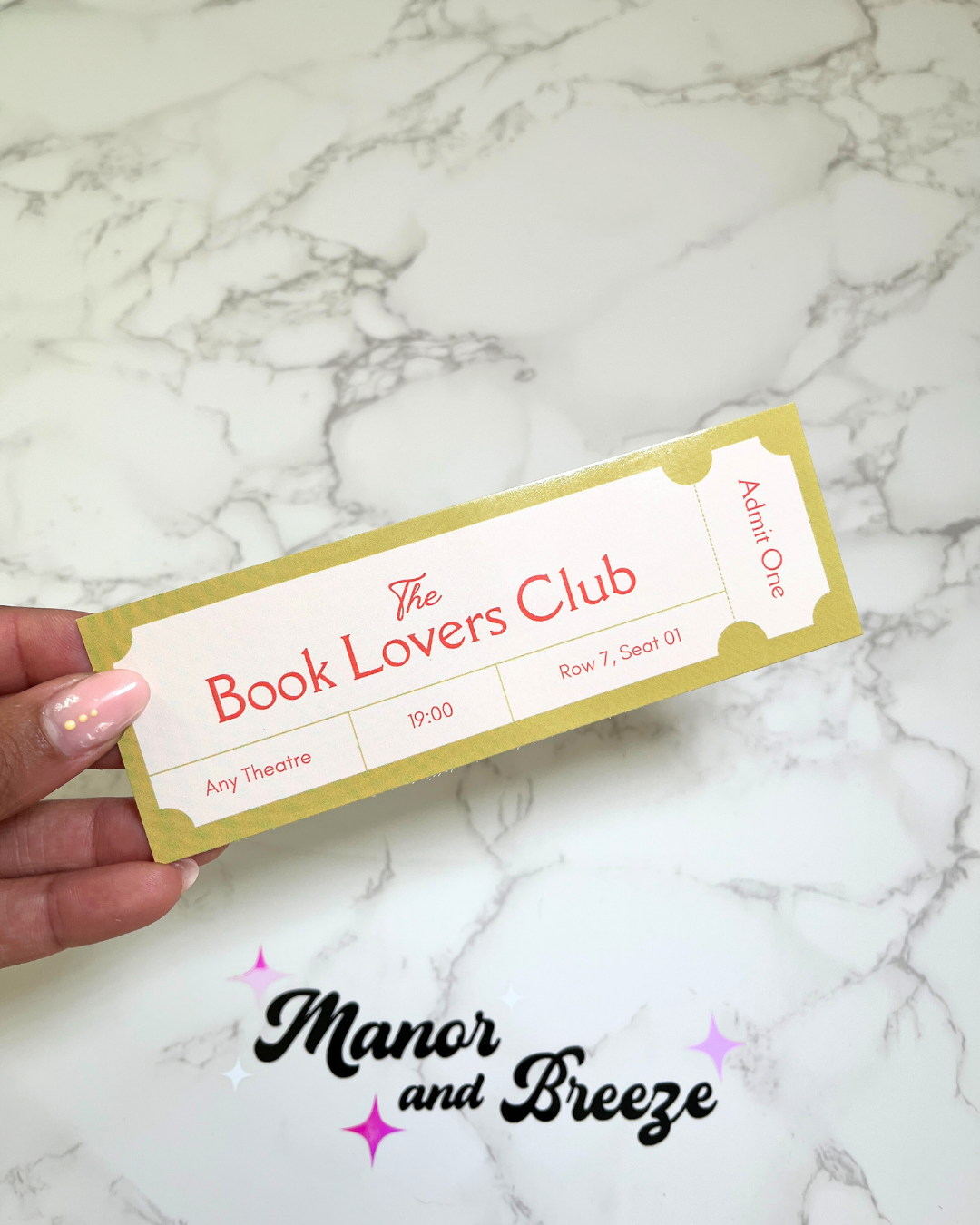 A pistachio green bookmark with 'The Book Lovers Club' text and a glossy finish, held by a hand against a marble background.