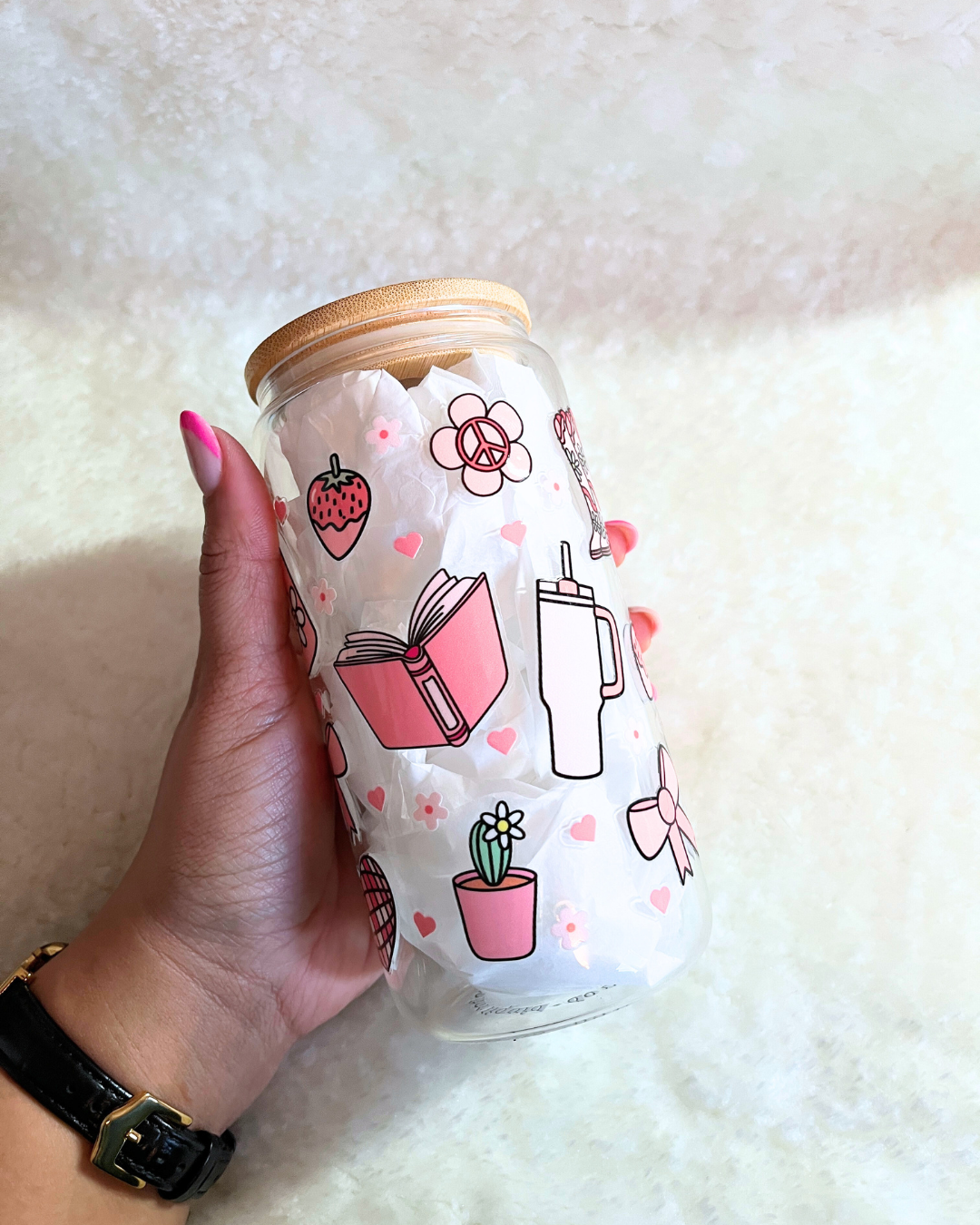 Hand holding a glass jar with pink illustrations on a white background