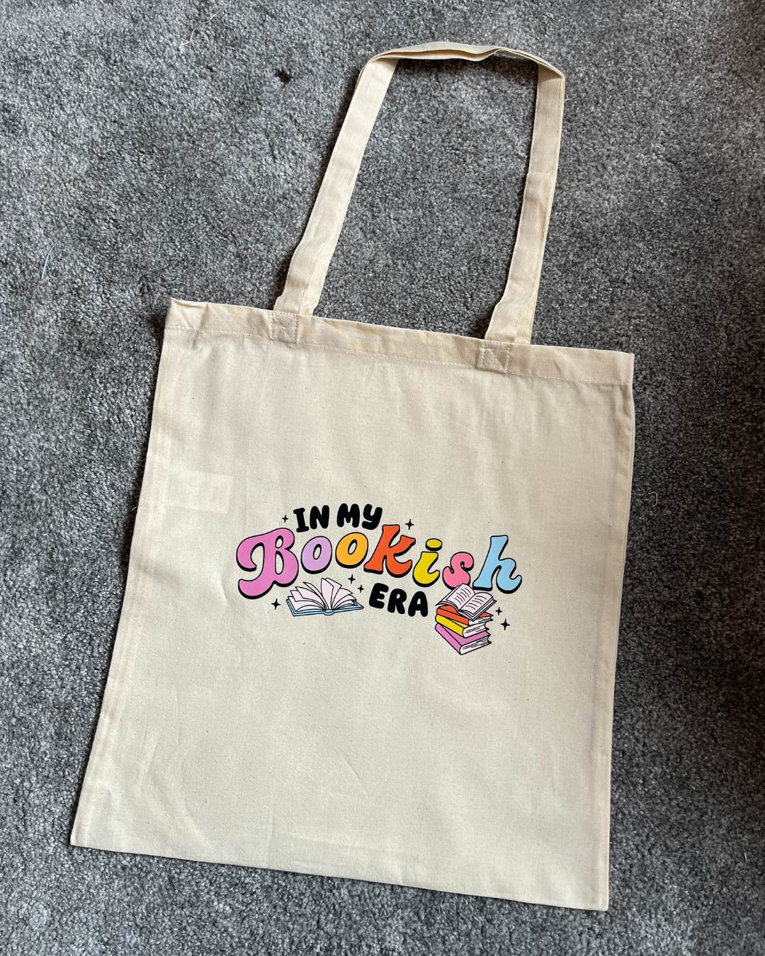 A beige cotton tote bag with the text 'In my bookish era' printed on the front.