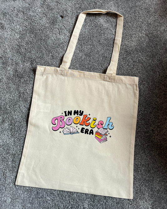 A beige cotton tote bag with the text 'In my bookish era' printed on the front.
