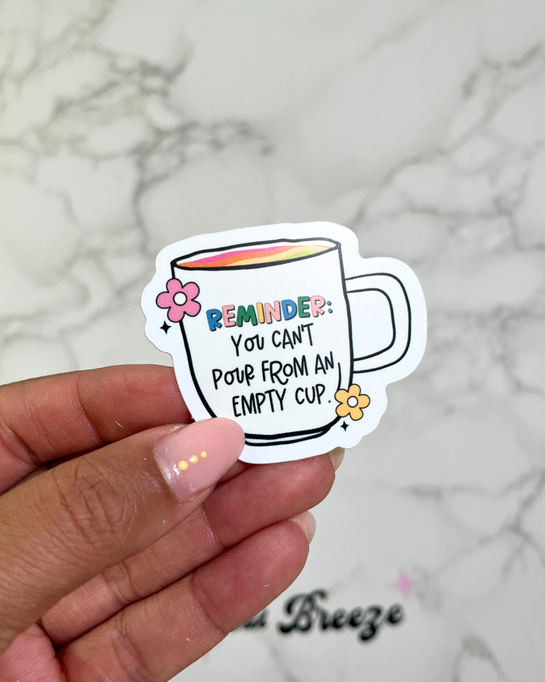 A hand holding a sticker with an illustration of a cup and flowers, and the text 'REMEMBER: You can't pour from an empty cup'.