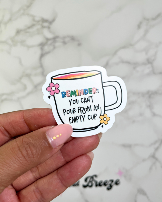 A hand holding a sticker with an illustration of a cup and flowers, and the text 'REMEMBER: You can't pour from an empty cup'.