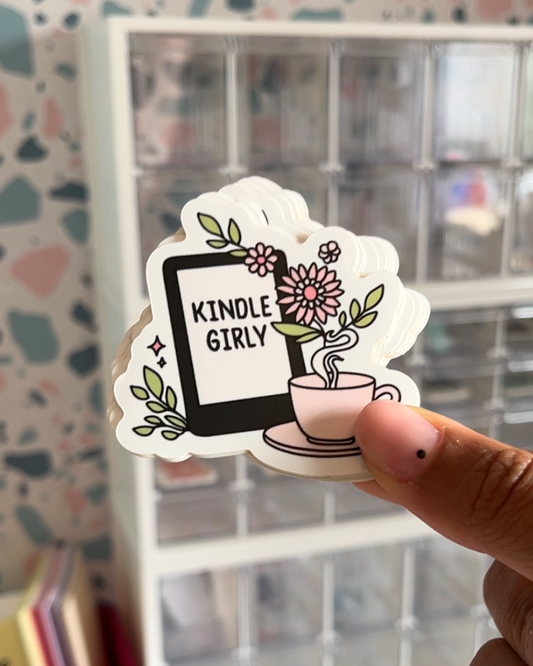 A sticker with an illustration of a character holding a cup and a Kindle, with the text 'KINDLE GIRLY' and floral elements.