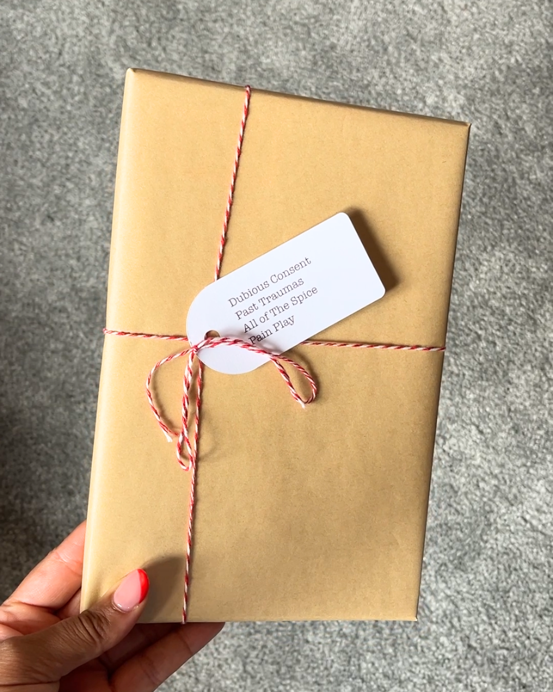 A book wrapped in brown paper with a red ribbon and a white label tag on the front cover, held in a person's hand.
