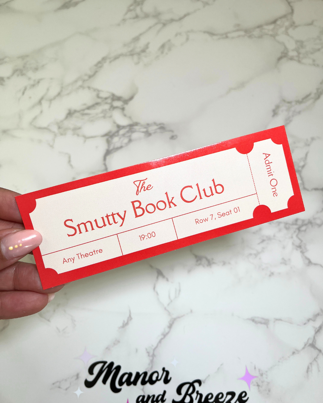 A hand holding a red bookmark with 'The Smutty Book Club' text 