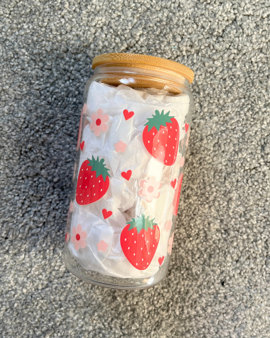 A glass drinking jar with a bamboo lid, decorated with a pattern of strawberries, pink flowers, and pink hearts.